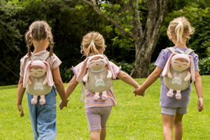 Three children holding hands with  bunny backpacks featuring cartoon characters outdoors.