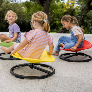 Three children sitting on colourful  spinning chairs outdoors.